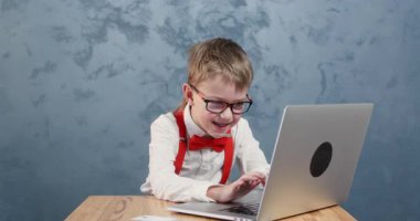 Gözlüklü çocuk bilgisayarında el sallayarak video çağrısı yapıyor. Pantolon askısı ve papyon takan gözbebeği bilgisayardan mesaj yazar