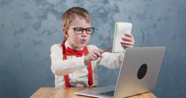 Öğrenci not defterindeki düzeltmeleri gözden geçiriyor. Gözlüklü, papyonlu ve pantolon askısı takmış bir öğrenci, yazıları okur ve düzenler.