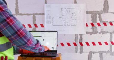 İnşaatçı bilgisayarla apartman planlarını analiz ediyor. Uzman dizüstü bilgisayardaki yazılımı yapılandırıyor ve yenileme çalışmalarına geniş salonda başlamaya hazırlanıyor.