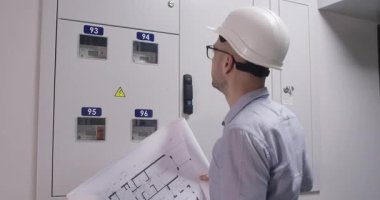 Gözlüklü adam, kağıt zemin planını inceleyip elektrik panelinin yerini kontrol ediyor. Dairenin onarım çalışmalarına başlamadan önce özel nesneler üzerinde çalışan miğfer mühendisi