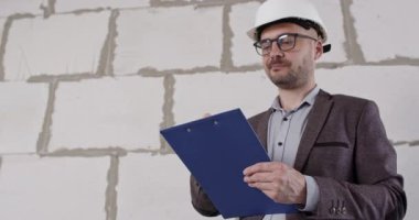 Ceketli mühendis, gelecekteki görevlere şaşırarak tepki verir. Profesyonel olarak yenileme hizmetlerinin fiyatlarını analiz eder ve geniş bir salonda duran notlar alır.