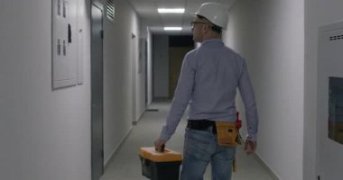 Sert şapkalı bir adam, dairelerin kapılarını kontrol eder ve adrese ulaşır. Mühendis, uzun bina koridorunda yürüyen aletlerle bavulu tutuyor.