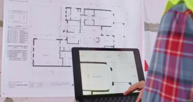 Uzman, yenilemeden önce duvarda ve ekranda kat planı üzerinde çalışıyor. Adam dizüstü bilgisayarla daire düzeni ve bina özellikleri hakkında ayrıntılı bilgi almak için çalışıyor