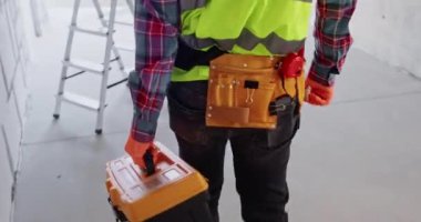 Uzman, yenileme alanına gelip özel alet çantasını açıyor. İnşaatçı, özel ekipman kullanılarak geniş apartman binasında işe başlamaya hazırlanıyor