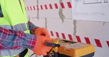 Adam alet kutusunu kapatıp işini bitirip apartman çıkışına doğru gidiyor. İnşaatçı, duvardaki kat planının önünde duran işi tamamlamak için özel araç çantası kullanır