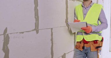 İnşaatçı, apartman yenileme işleminden önce hazırlık işlerini yapar. Adam kağıda not alır ve beton blokların yanında çalışmaya başlar.