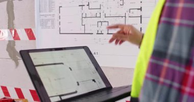 Uzman, kat planlarını çalışmak için bilgisayar üzerinde program kullanıyor. İş kıyafetleri ustası dizüstü bilgisayarı elinde tutuyor ve yenilenmiş dairenin planına aşina oluyor.