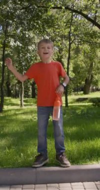 Gündelik giysiler içinde gülümseyen liseli çocuk elinde su şişesiyle kaldırımın kenarına atlıyor. Sevimli çocuk neşeyle gülüyor ve neşeli bir enerjiyle zıplıyor. Dikey çekim