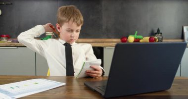 Küçük okul çocuğu not defterine notlar yazar ve dizüstü bilgisayarına düşünce ve şaşkınlık anını belirten notlar yazar. Bilgisayarı aç ve masadaki kağıtlar çalışma oturumunu gösteriyor