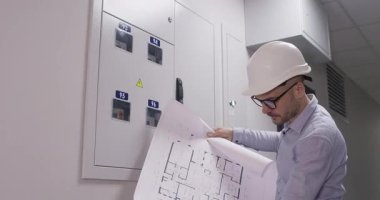 Miğfer ustası, açılıp kapanmayan kağıt düzenini dikkatlice inceler. Uzman, koridorda yenileme işlemine başlamadan önce kabinenin kat planına bakıyor