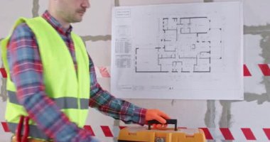 Adam koridorda duran alet çantasından mezurayı alıyor. Eldiven mühendisi nesnelerin uzunluğunu ölçmeye ve apartman yenileme çalışmalarına başlamaya hazırlanıyor.