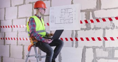 Mühendis dizüstü bilgisayarla dairenin planını analiz ediyor. Uzman, küçük merdiven üzerinde oturan yenileme ve çalışma düzeni özelliklerine başlamaya hazırlanıyor