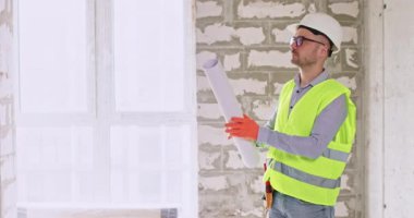 İnşaatçı, tadilattan önce kağıt döşemeleri açıyor ve boş odayı inceliyor. Sert şapka mühendisi, gelecekte yapılacak işlerin kapsamını değerlendiren apartman şeması üzerinde çalışıyor.