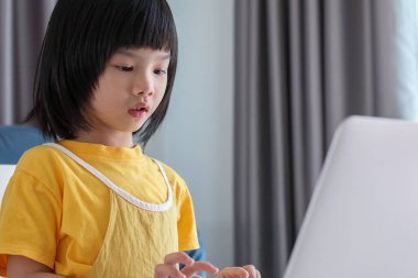 Küçük Asyalı kız öğrenci çevrimiçi evde dizüstü bilgisayar kullanıyor.