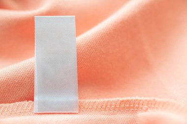Blank white laundry care clothes label on pink fabric texture background