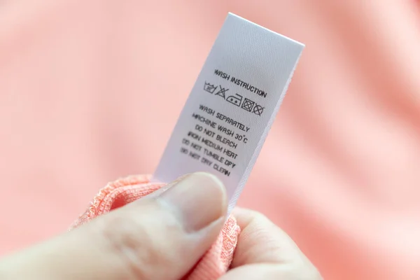 Stock image Hand hold and reading at white laundry care washing instructions clothes label on pink shirt