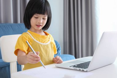 Küçük Asyalı kız öğrenci çevrimiçi evde dizüstü bilgisayar kullanıyor.