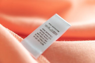 White laundry care washing instructions clothes label on pink cotton shirt