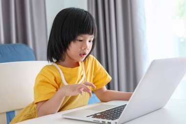 Küçük Asyalı kız öğrenci çevrimiçi evde dizüstü bilgisayar kullanıyor.