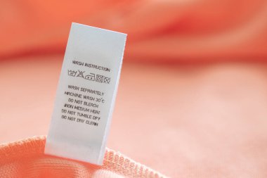 White laundry care washing instructions clothes label on pink cotton shirt