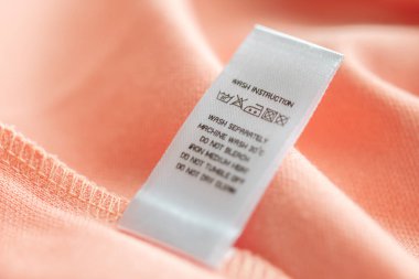 White laundry care washing instructions clothes label on pink cotton shirt