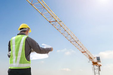 İnşaat mühendisi koruyucu miğfer ve inşaat alanındaki planlar üzerinde çalışıyor.