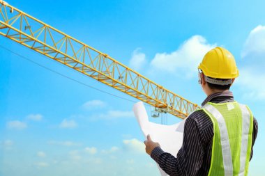 İnşaat mühendisi koruyucu miğfer ve inşaat alanındaki planlar üzerinde çalışıyor.