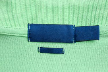 Yeşil gömlek kumaş arka planında boş mavi çamaşırhane kıyafetleri etiketi