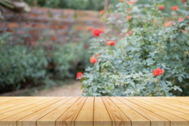 Ürün gösterimi için arkaplanı bulanık gül bahçeli boş tahta masa