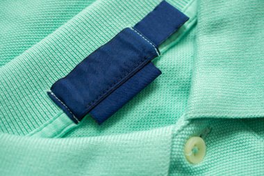 Yeşil gömlek kumaş arka planında boş mavi çamaşırhane kıyafetleri etiketi