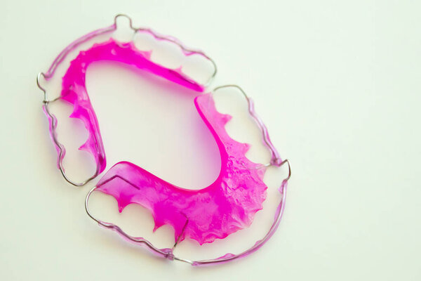 Розовый акриловый зубной протез на белом фоне