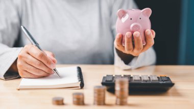 woman hand holding piggy bank on wood table, saving money wealth and financial concept, Business, finance, investment, planning. businessperson short note an accounting receive, send of money to bank