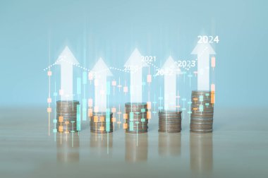 Tahta bir masanın üzerindeki yüksek miktardaki madeni para yığını iş ve finans özünü temsil ediyor, tasarruf yapmanın, para idaresinin ve akıllıca yatırım kararları vermenin önemini vurguluyor. Büyüyen grafik konsepti