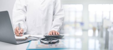 Sağlık sektörü finans kavramı. İş kadını ya da doktor hastanedeki insanlar tıbbi malzemelerin maliyetini kontrol etmek için muhasebecilerle irtibat kuruyor. stetoskop, çizelge, evrak, dizüstü bilgisayar, güvertede grafik