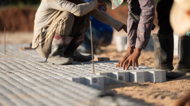 Kaldırım taşları konsepti kuruluyor. Çalışkan bir adam inşaat alanında çalışıyor, inşaat alanında dayanıklı ve iyi döşenmiş bir zemin oluşturmak için kaldırım taşları ve çimento döşüyor.