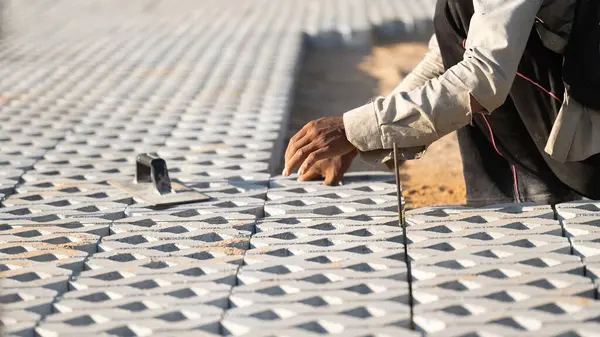 Kaldırım taşları konsepti kuruluyor. Çalışkan bir adam inşaat alanında çalışıyor, inşaat alanında dayanıklı ve iyi döşenmiş bir zemin oluşturmak için kaldırım taşları ve çimento döşüyor.