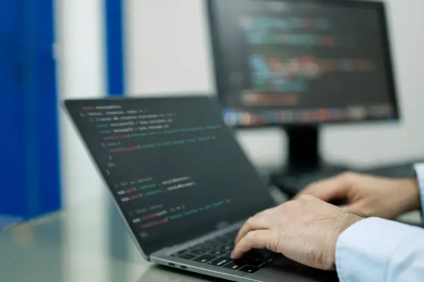 Geliştirici siyah ekranlı bir dizüstü bilgisayarda yazıyor. Laptop üzerinde bir sürü kod olan bir sayfayı açıyor. Adam işine odaklanmış, muhtemelen bir proje üzerinde çalışıyor ya da programlıyor.