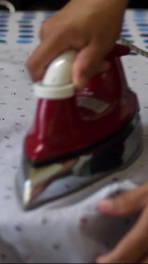 Bir kişi üzerinde desen olan bir parça elbiseyi ütülüyor. Ütü kırmızı ve kişi siyah bir gömlek giyiyor.