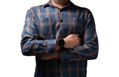 Ekose gömlek ve saat giyen bir adam. Kollarını kavuşturmuş duruyor. Gömlek mavi ve turuncu.