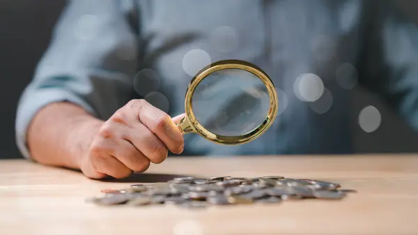 Ticarette bir kişi büyüteç altında sikkeleri titizlikle analiz eder, yenilikçi kavramları ve stratejileri araştırır, başarılı çözümler ve finansal büyüme için çığır açan fikirler keşfeder.