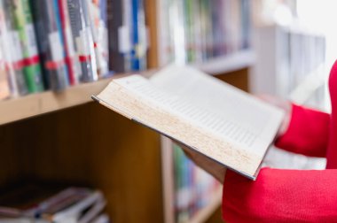 Kütüphanede kitaplıklarla çevrili bir kadın öğretmen, üniversite öğrencilerini edebiyat, ders kitapları ve bilgilerden yararlanarak öğrenim deneyimlerini geliştirmek için eğitir..