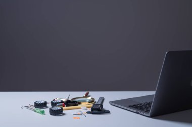 Kök eğitim konsepti. Dizüstü bilgisayar, çeşitli araç gereçleri ve parçaları etrafa saçılmış bir masada duruyor. Sahne, muhtemelen elektronik veya mekanik çalışmalar içeren yaratıcı veya teknik bir proje öneriyor