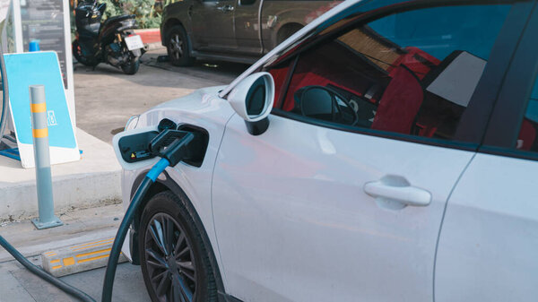 Концепции устойчивого развития. Электромобили. Белый автомобиль заряжается на зарядной станции.