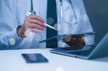 Bir doktor not almak için bir tablet ve bir kalem kullanıyor. Tablet, hakkında bir sürü bilgi içeren bir sayfayı açıyor. Doktor tablete odaklanmış durumda.