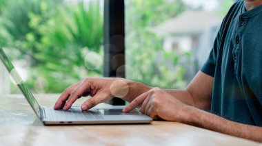 Parlak yeşil bir ortamda bir kişi aktif olarak dizüstü bilgisayarda yazı yazıyor. Sahne, doğayla harmanlanmış modern teknoloji ve uzaktan çalışmanın özünü yakalıyor.