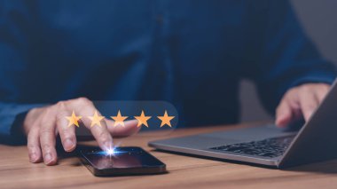 Bir kişi dizüstü bilgisayar ve cep telefonu kullanıyor ve cep telefonunun yıldız derecesi, değerlendirmesi, değerlendirmesi, tatmini, başarısı, kalitesi, deneyimi var.