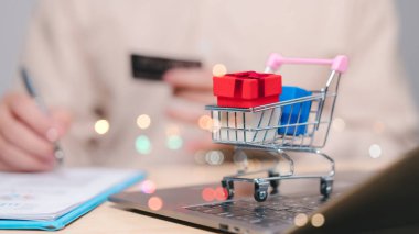 Renkli hediyelerle dolu minyatür alışveriş arabası dizüstü bilgisayarın üzerinde oturuyor ve festival sezonlarında online alışveriş ve hediye verme sevincini simgeliyor.