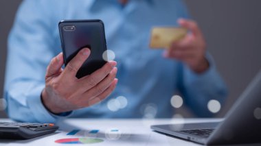 Çevresindeki finansal belgelerle çevrili akıllı telefon ve kredi kartıyla online alışverişe girişen kişi, günümüzde hızlı gelişen dünyada dijital işlemlerin kolaylığını vurguluyor