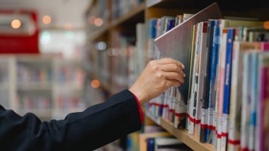 Gençlik öğrenme konsepti. Kütüphane rafındaki kitap için el uzanıyor, bilgi ve edebiyat dolu dünyada keşif ve keşif anı