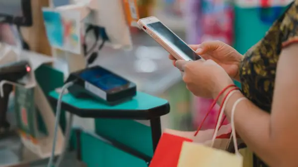 Alışveriş yapan kişi kasada ödeme yapmak için akıllı telefon kullanıyor, günlük alışverişte dijital işlemlerin kolaylığı